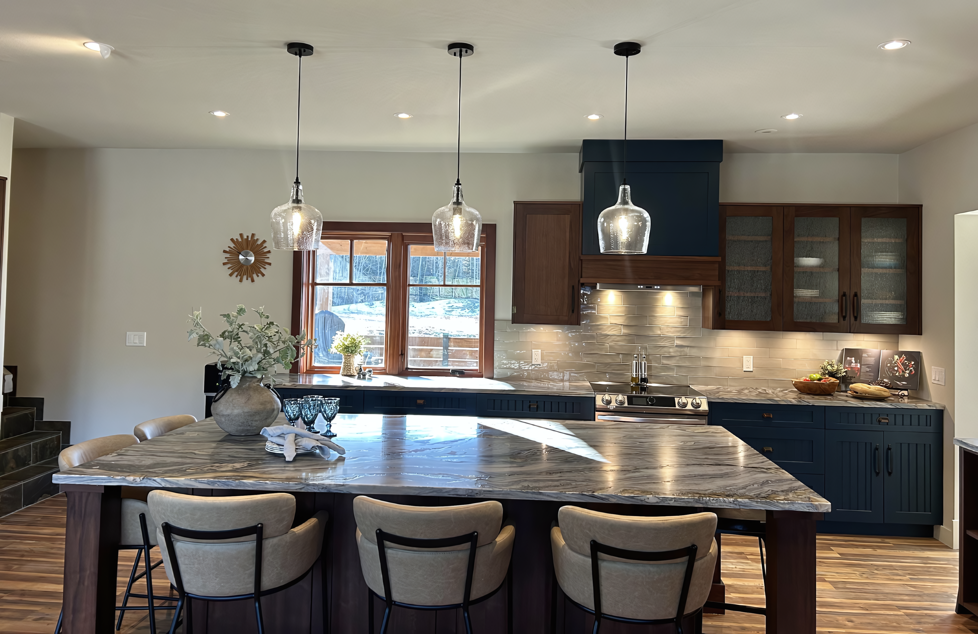 Warm modern open-concept kitchen featuring navy blue lacquer base cabinets, a massive walnut-clad island with a heavily veined quartzite countertop, and vertical-grain walnut upper cabinets.