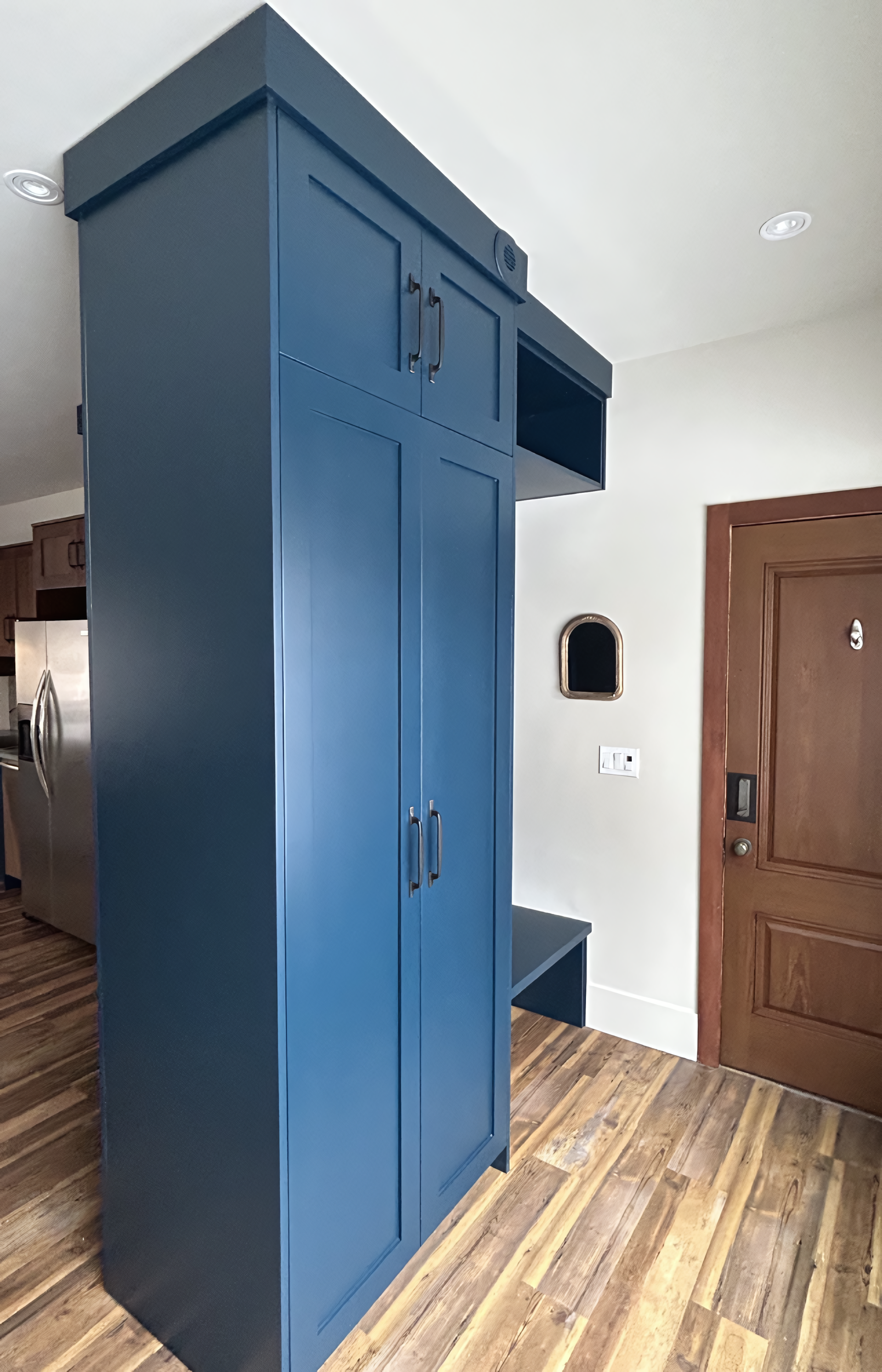 Custom built-in entryway storage in a deep blue finish, featuring full-height shaker cabinetry, an integrated bench, vertical back paneling with hooks, and an upper open shelf for organized mudroom functionality.