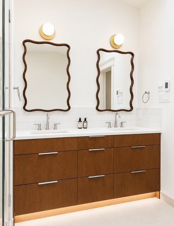 Modern double vanity with warm wood slab drawer fronts, white quartz countertop, vertical stack tile backsplash, two organic-shaped dark-framed mirrors, and integrated LED toe-kick lighting.