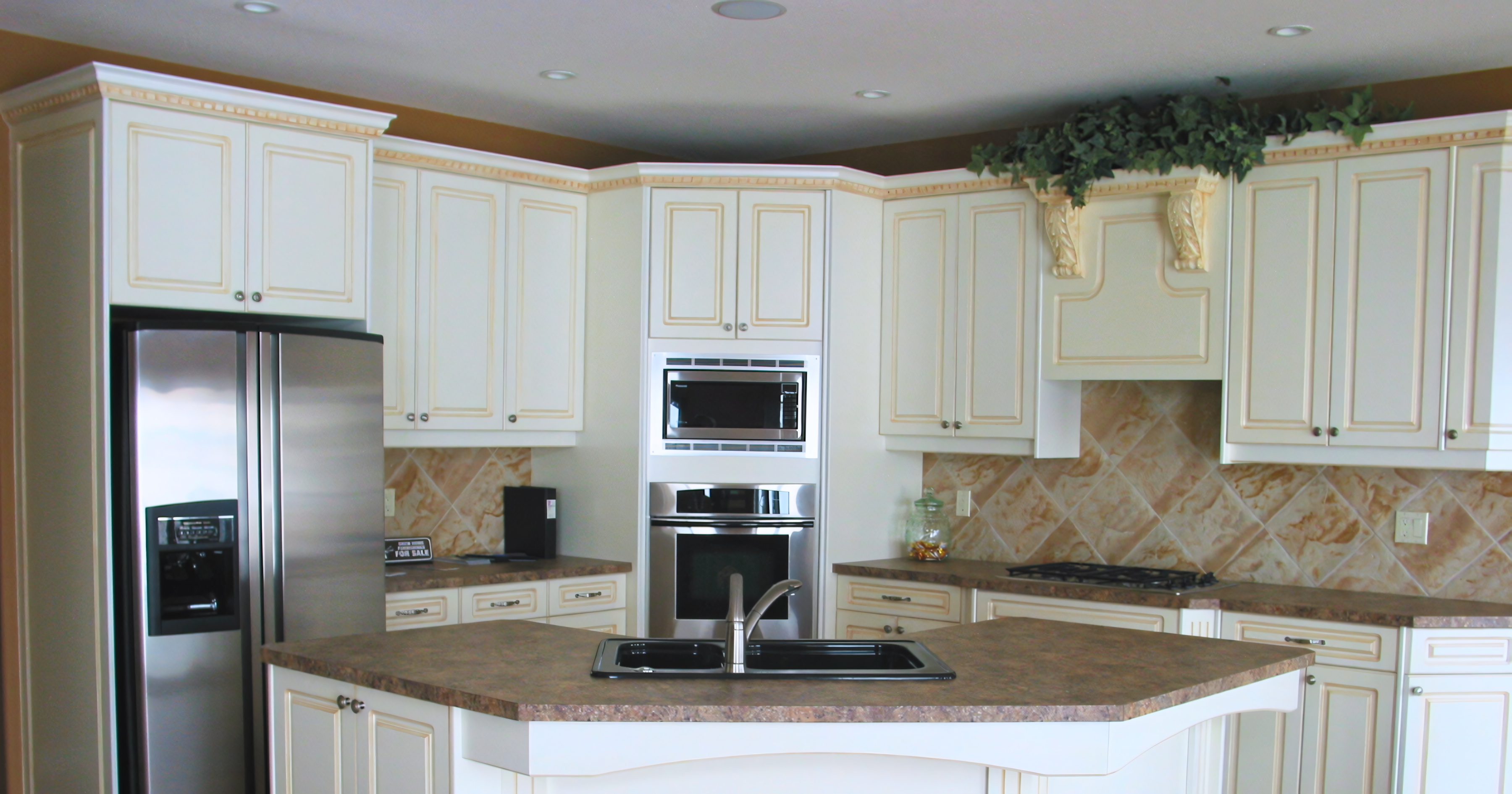 Modern transitional "tuxedo" kitchen featuring a high-contrast palette of white shaker-style perimeter cabinetry and a dark stone-topped island with natural wood-toned base units. The layout highlights premium utility with a black apron-front farmhouse sink, a built-in induction or glass cooktop integrated into the island, and a stainless steel dishwasher. High-end finishes include a dark brown brick-pattern subway tile backsplash, white marble-look quartz perimeter countertops, and modern black bar pulls.