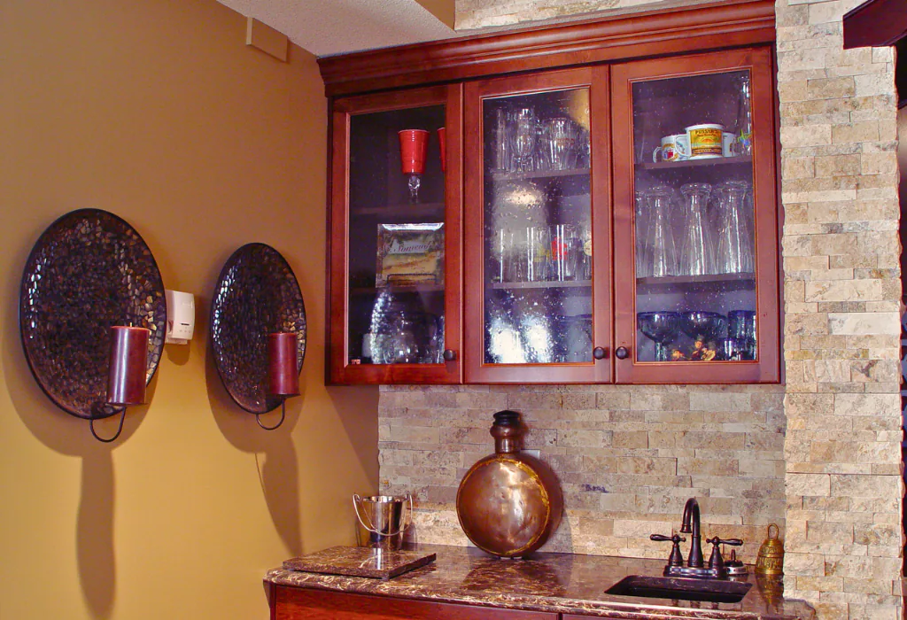 Traditional home bar featuring custom cherry-finished upper cabinets with glass mullion inserts and a matching architectural crown moulding.