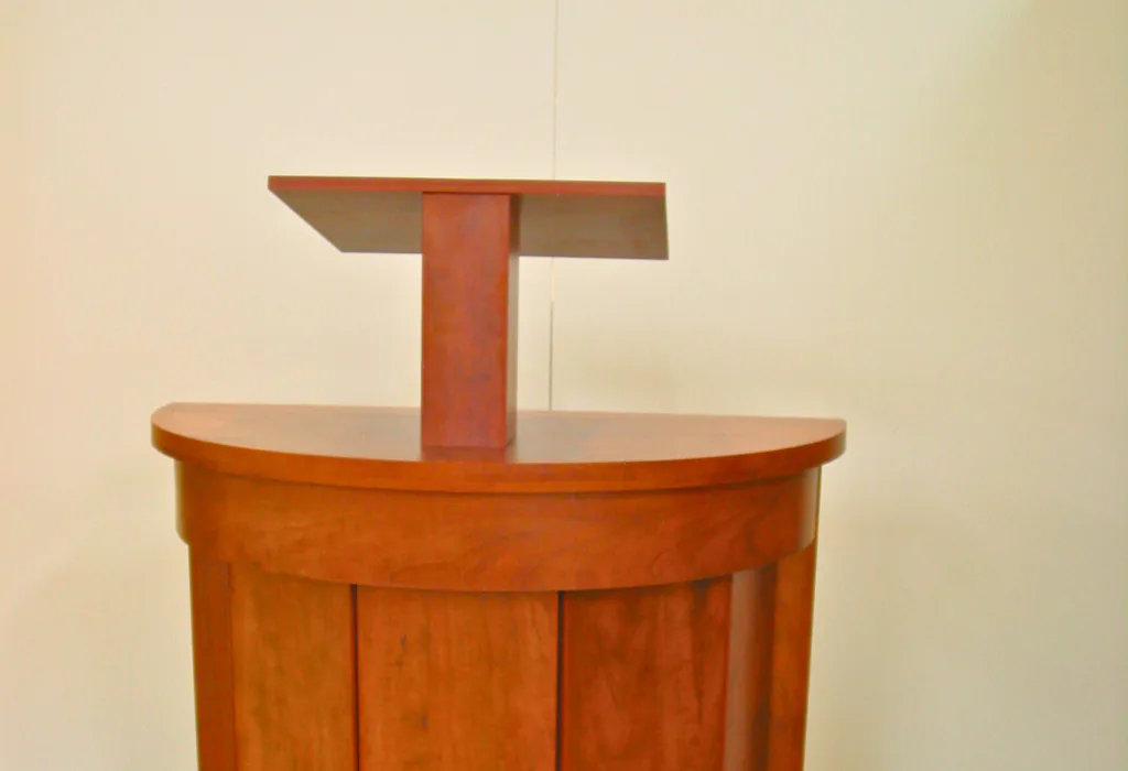 Custom cherry-stained wooden pedestal with a rounded vertical-stave base and an elevated, matching reading platform.