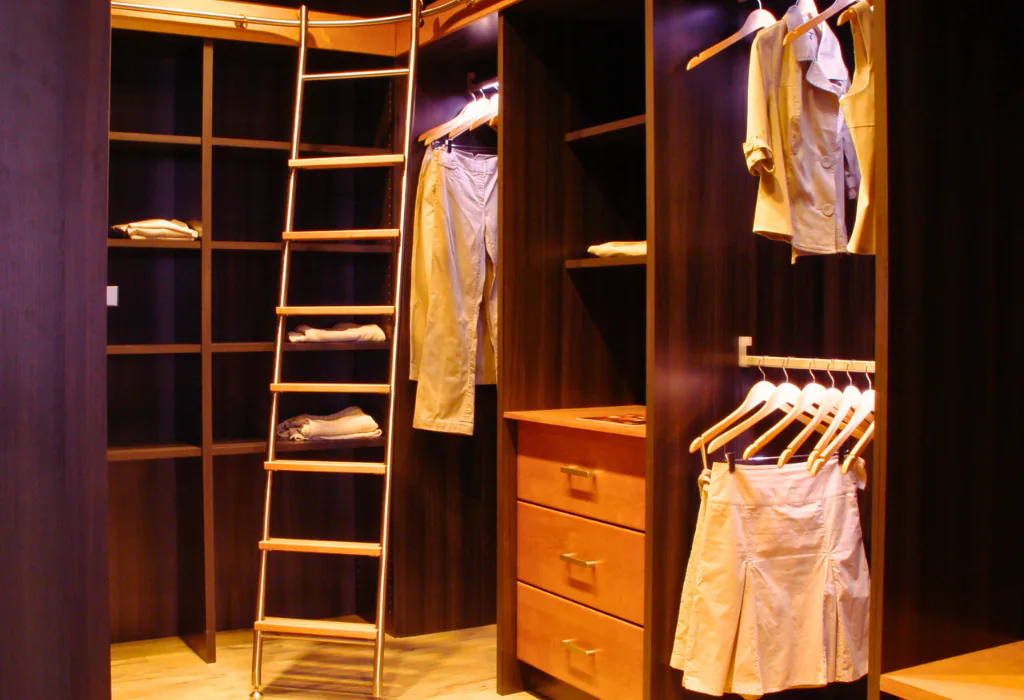 Custom dark espresso-stained walk-in closet featuring floor-to-ceiling shelving, integrated LED channel lighting, and a wooden library ladder hooked onto a top metallic rail.