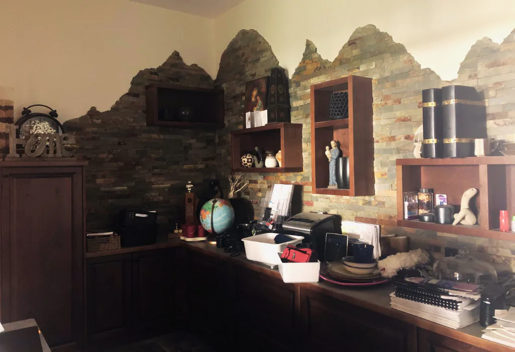Professional home office featuring custom warm-toned wood cabinetry and floating shelves integrated into a rugged natural stone-veneer accent wall.