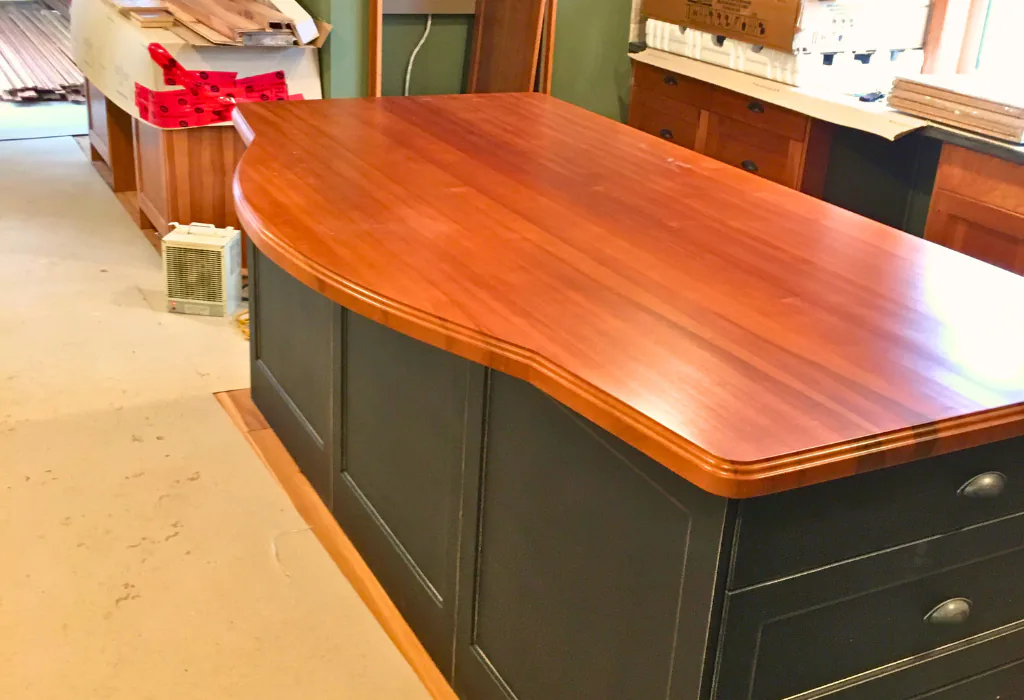 Custom kitchen island in a workshop featuring a rich, warm wood-grain countertop over a dark charcoal-painted cabinet base.