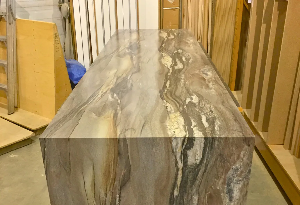Behind-the-scenes shop shot of a custom wood veneer kitchen island showing a precisely mitered waterfall gable end during final assembly.