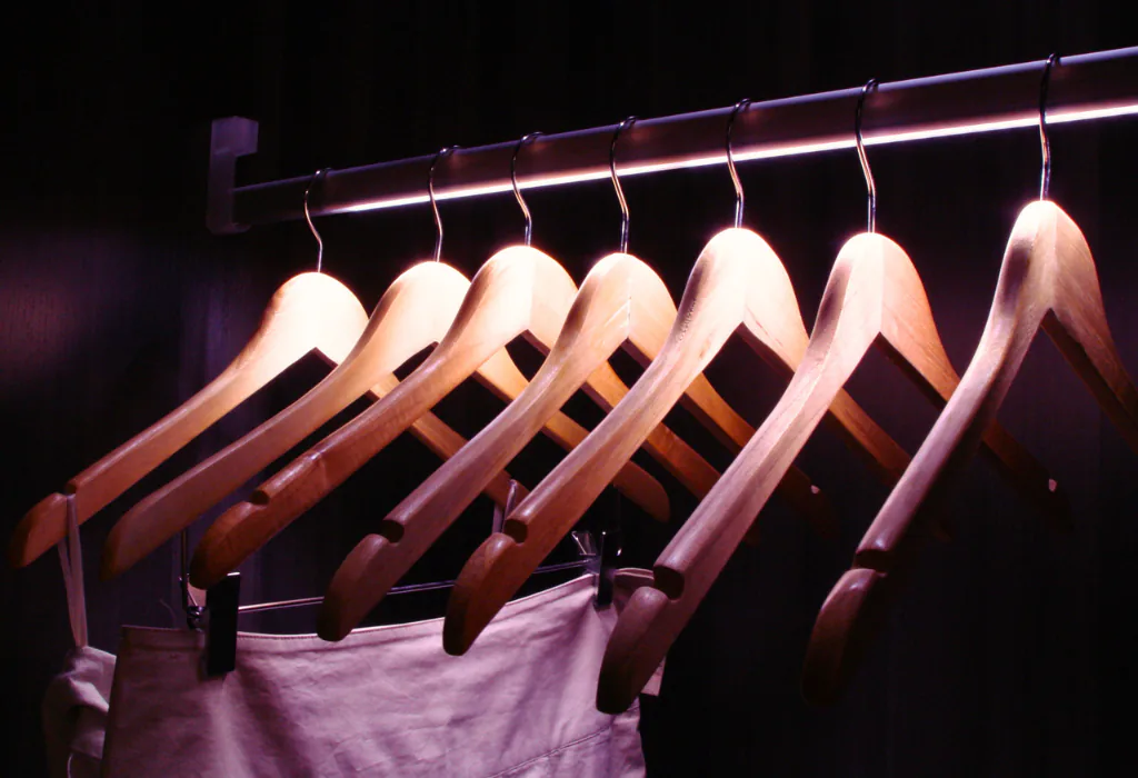 Close-up of a custom metallic closet hanging rod with an integrated recessed LED light strip illuminating wooden clothing hangers.