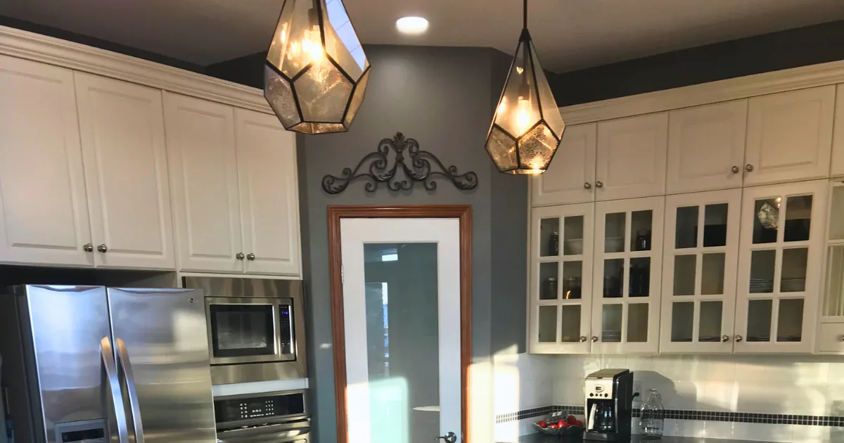 Classic white kitchen highlighting custom glass-insert upper cabinets, built-in double wall oven openings, and a matching custom pantry door with a frosted glass pane.
