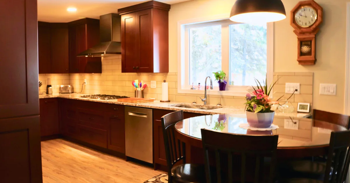 Warm, inviting kitchen featuring dark wood cabinetry, an under-cabinet task lighting setup, and a sage green textured glass tile backsplash reflecting natural window light.
