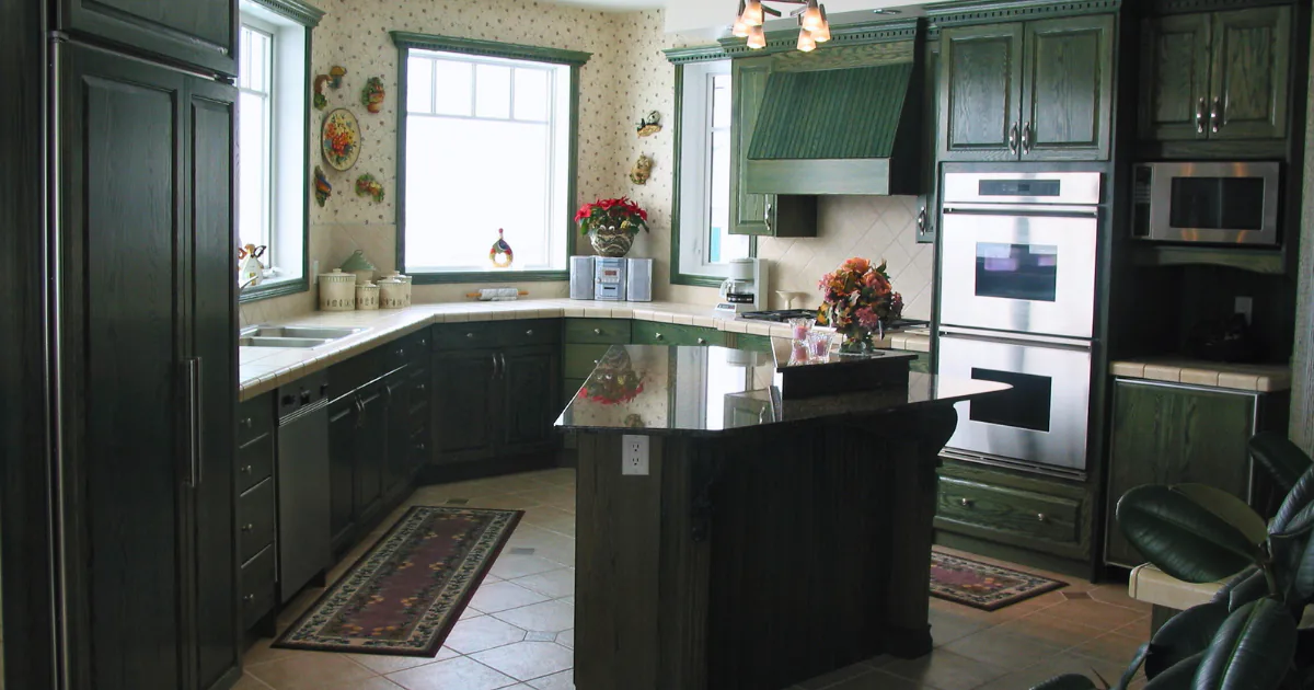 ransitional kitchen with off-white perimeter cabinets, a contrasting sage green range hood and accent cabinetry, a central island, and warm hardwood flooring.